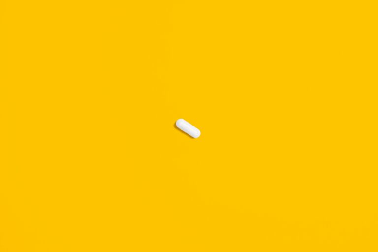 A single white pill lies against a bright yellow background, highlighting its simplicity and focus.